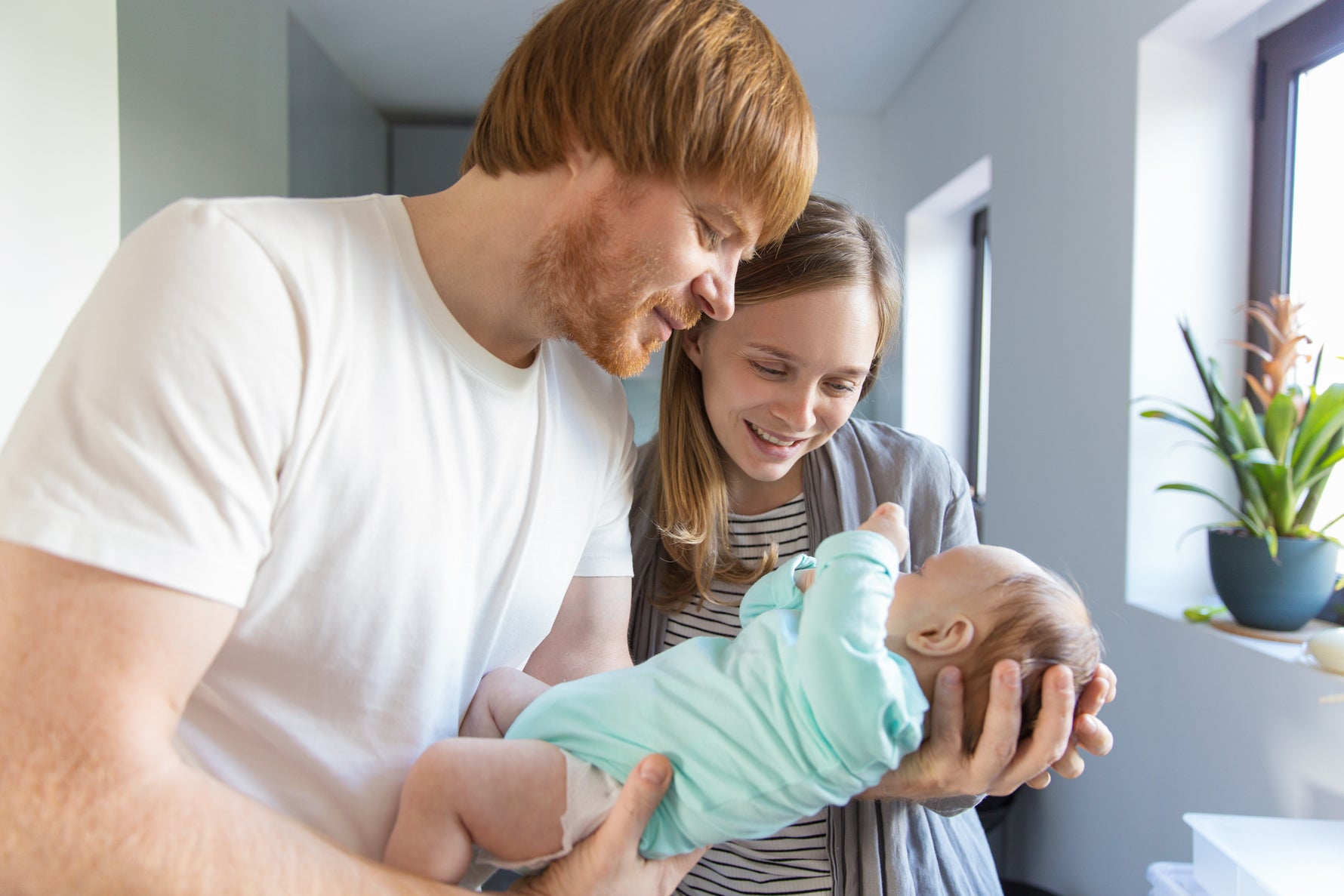 Happy new parents joyfully cuddling their newborn baby in a bright and loving home environment.