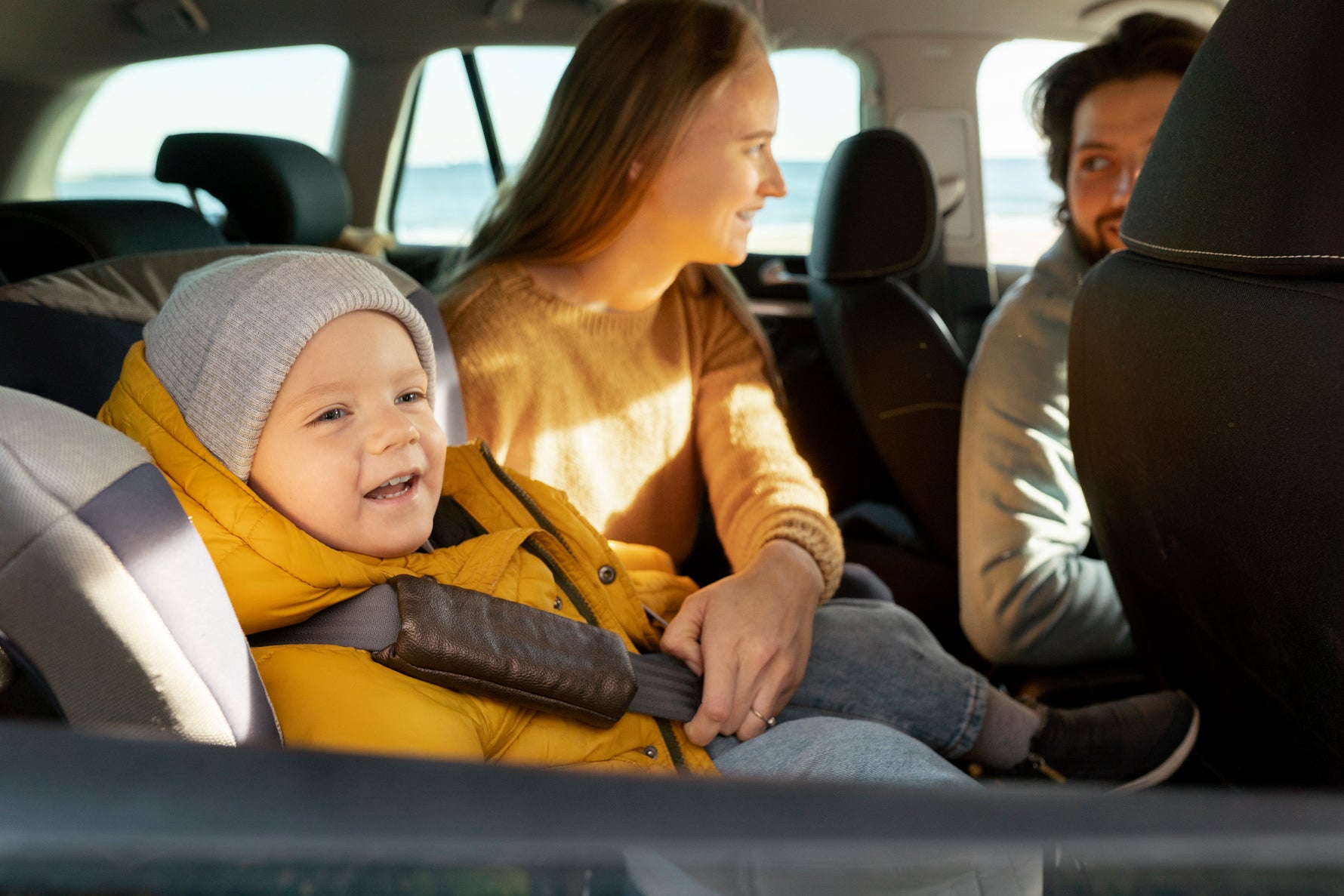 A happy toddler safely secured in a car seat, enjoying a family road trip with smiling parents.